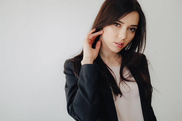 Menina emocional atraente nova na roupa do negócio-estilo em um fundo branco liso em um escritório ou público sozinho
 - Foto, Imagem
