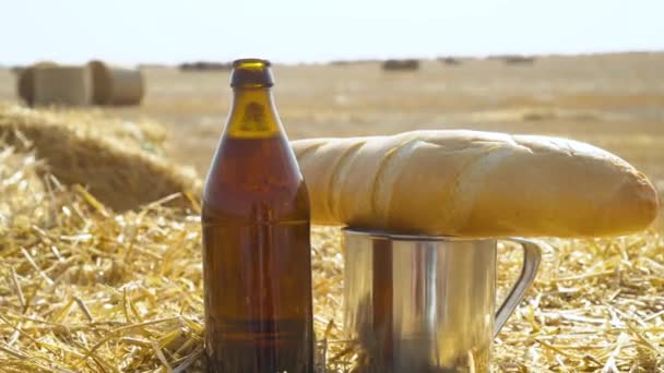Beer, bread and metal glass on a wheat field with bales. Fresh beer, solar field - Πλάνα, βίντεο
