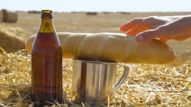 Beer, bread and metal glass on a wheat field with bales. Man takes bread - Footage, Video