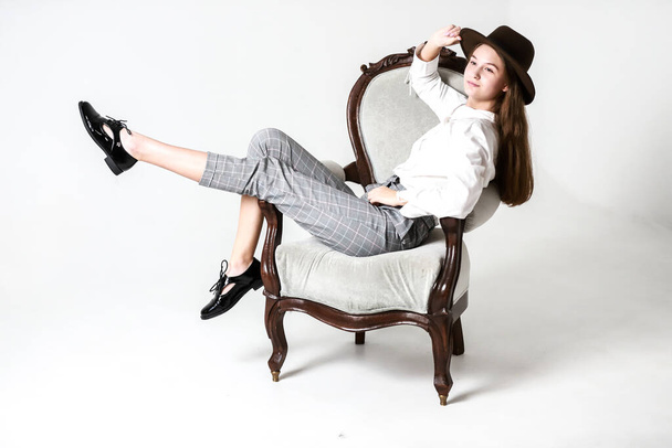 mooi meisje in een hoed zit in een stoel - Foto, afbeelding