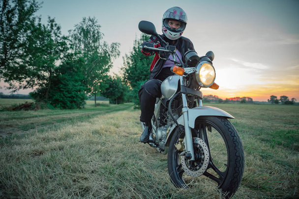 jovem mulher atraente na motocicleta na estrada de terra ao pôr do sol
 - Foto, Imagem
