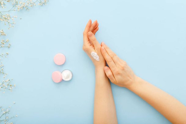 Hand cream, female hands applying organic natural cream cosmetics on a pastel blue colored background. Skin care cream in jar for hands,body. Flat lay moisturizing cream for soft skin, health, beauty - 写真・画像