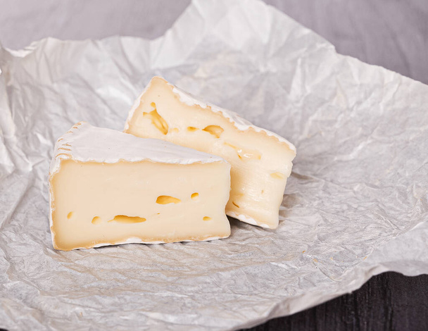 queijo brie em papel branco em uma mesa de madeira
 - Foto, Imagem