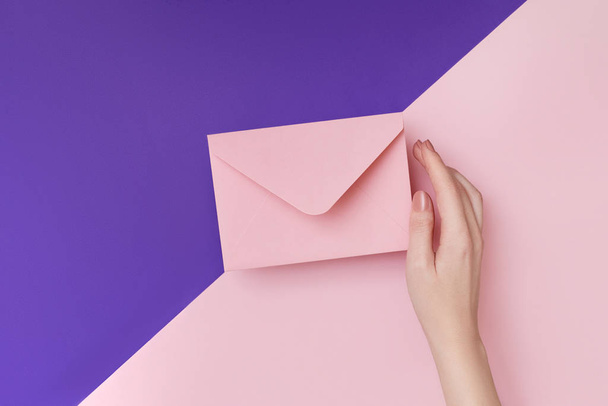 ダブルカラーのピンクとバイオレットの背景に女性の手にピンクの封筒。メールのコンセプト - 写真・画像