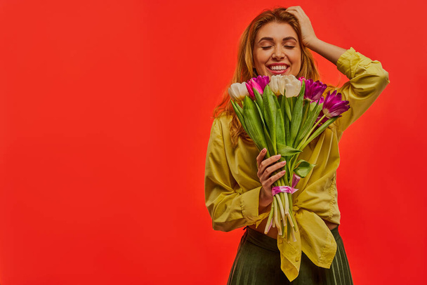 Lady with a smile with fair wavy hair in a yellow blouse has a bouquet of flowers and  looks at the camera. - Foto, imagen