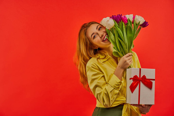 Lady with smile with fair wavy hair hugs a bouquet of flowers and holds a gift box. - Fotoğraf, Görsel