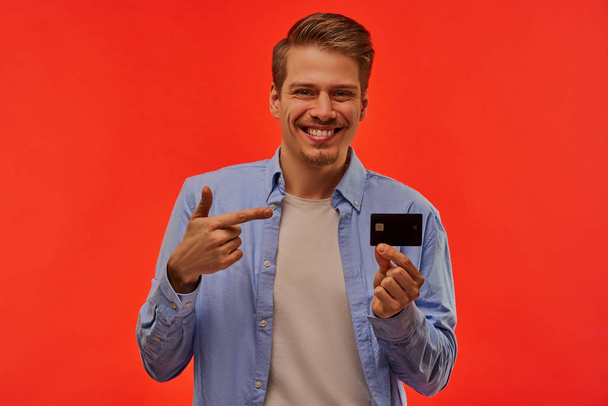 Happy guy in one hand holds a credit card and points to it. - Foto, Imagem