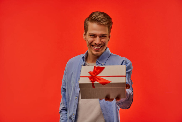 A guy with wide smile with white box with a red bow in hand. - Foto, Imagen