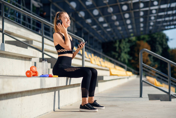Attractive young healthy sportswoman listens to music with earphones during training at the stadium. - Foto, imagen