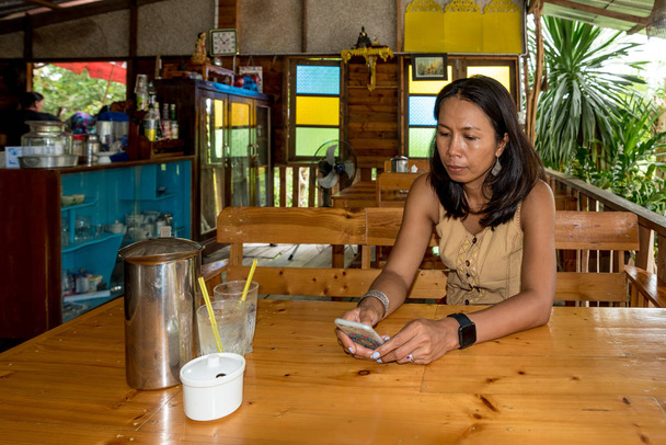 Vrouw aan tafel in café met mobiele telefoon in Pak nam Pram, Pranburi, Thailand - Foto, afbeelding