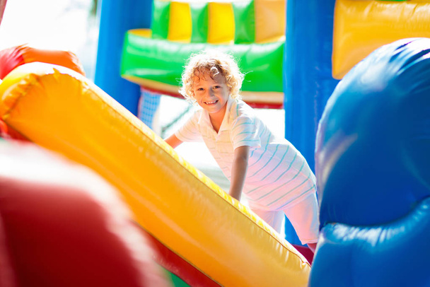 Child jumping on colorful playground trampoline. Kids jump in inflatable bounce castle on kindergarten birthday party Activity and play center for young child. Little boy playing outdoors in summer. - Photo, Image