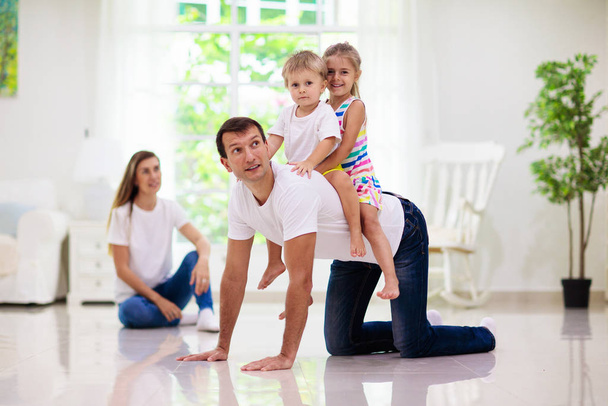 Happy young family with kids at home. Father, mother, daughter and son playing on the floor in living room. Mom, dad, little boy and girl holding pet cat. Parents and children play together. - Fotoğraf, Görsel