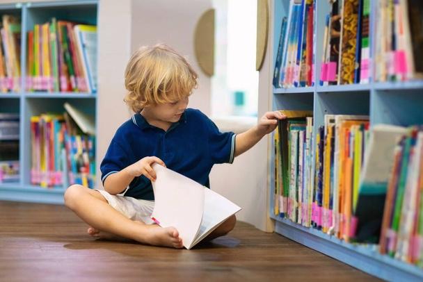 Ребёнок в школьной библиотеке. Дети читают книги. Мальчик читает и учится. Дети в книжном магазине. Умный умный дошкольник выбирает книги для заимствования. - Фото, изображение