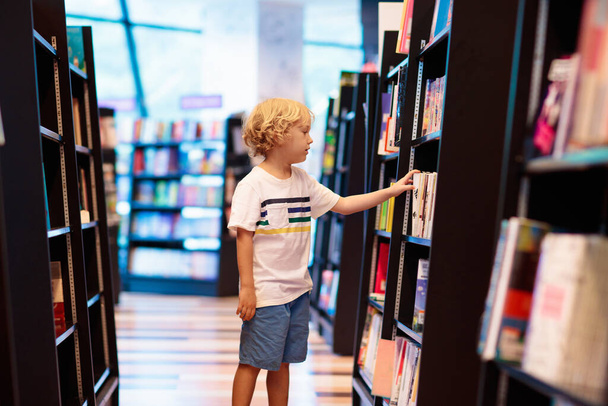 Dziecko w szkolnej bibliotece. Dzieci czytają książki. Mały chłopiec czyta i uczy się. Dzieci w księgarni. Inteligentny inteligentny przedszkolak wybiera książki do pożyczenia. - Zdjęcie, obraz