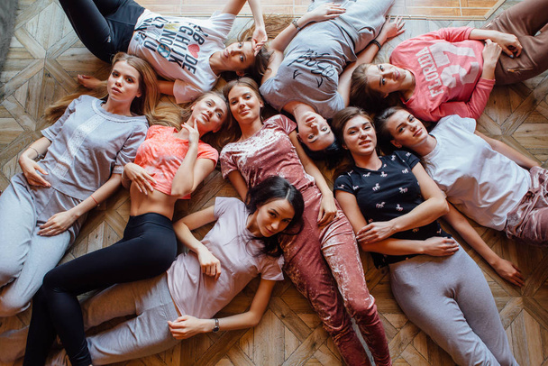 Widok z góry dziewięciu szczęśliwych pięknych kobiet leżących na podłodze poding i uśmiech. Piżama party - Zdjęcie, obraz