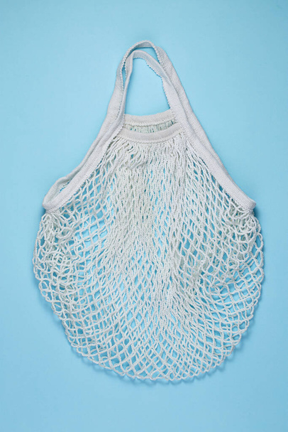 White cotton mesh bag on blue paper background. Reusable shopping bag on color background. Ecological, Zero waste concept. Top view, flat lay, copy space - Fotó, kép