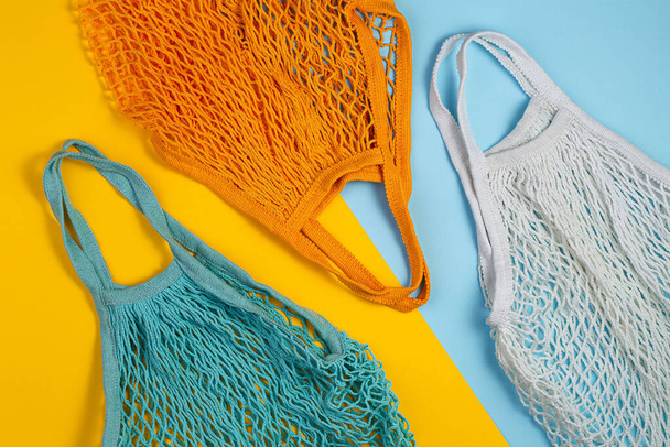 Zero waste concept. Three mesh shopping bags lie on yellow blue background. Eco friendly and reuse concept. Top view or flat lay - Фото, изображение