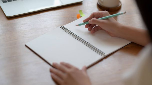 Close-up uitzicht op een vrouw schrijven op mock up notebook met laptop op houten bureau in eenvoudige werkplek - Foto, afbeelding