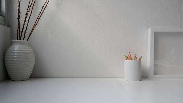Close up άποψη του ελάχιστου χώρου εργασίας με αντίγραφο χώρο, διακοσμήσεις και χρωματιστά μολύβια σε λευκό γραφείο με φόντο λευκό τοίχο - Φωτογραφία, εικόνα