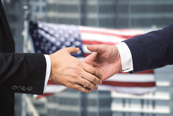 Potřesení rukou dvou podnikatelů na pozadí vlajky USA, podpis konceptu smlouvy, close up - Fotografie, Obrázek
