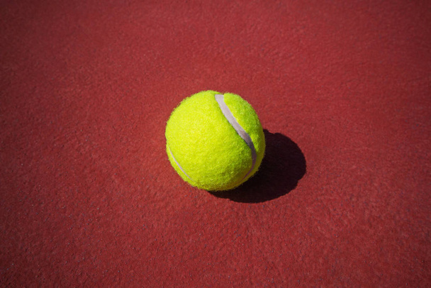 De tennisbal wordt op een rode vloer geplaatst. - Foto, afbeelding