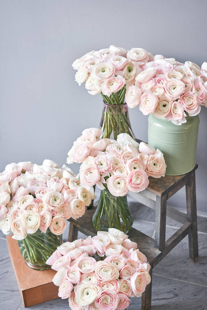Lot of flowers Persian buttercup. Bunch pale pink ranunculus flowers on light gray background. Glass vase on vintage wooden table. Wallpaper - Photo, Image