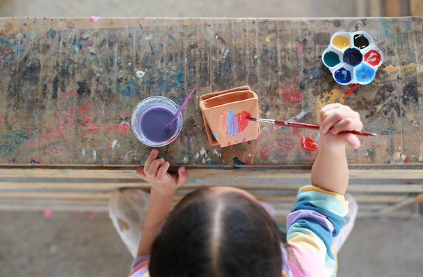 Asian little kid girl painting on earthenware dish. View on top. - 写真・画像