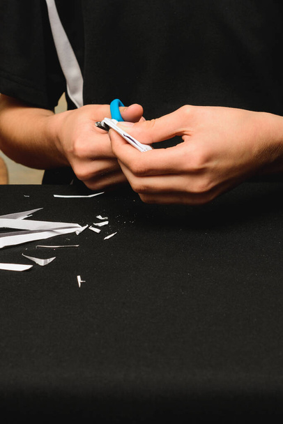 Το αγόρι διπλώνει και κόβει λευκό χαρτί με τα χέρια και το ψαλίδι του. 2020 - Φωτογραφία, εικόνα