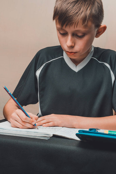 Ein Junge sitzt an einem Tisch und zeichnet Bleistifte auf weißem Papier. - Foto, Bild