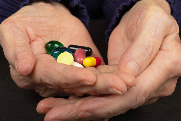 Φωτογραφία από ένα ανώτερο ασθενή χέρι κρατώντας πολύχρωμα χάπια - Φωτογραφία, εικόνα