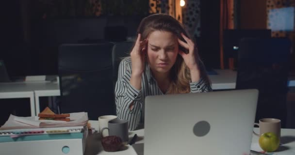 Front view of tired businesswoman massaging templates and forehead to concentrate while working long hours Exhausted girl using her computer at empty night office. Concept of overwork. - Footage, Video