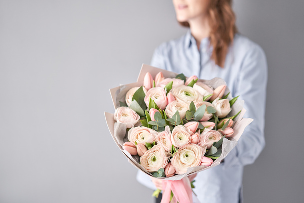 Ένα μάτσο ωχρές ροζ τουλίπες και ranunculus λουλούδια με πράσινο ευκάλυπτο. Η δουλειά του ανθοπώλη σε ανθοπωλείο. - Φωτογραφία, εικόνα