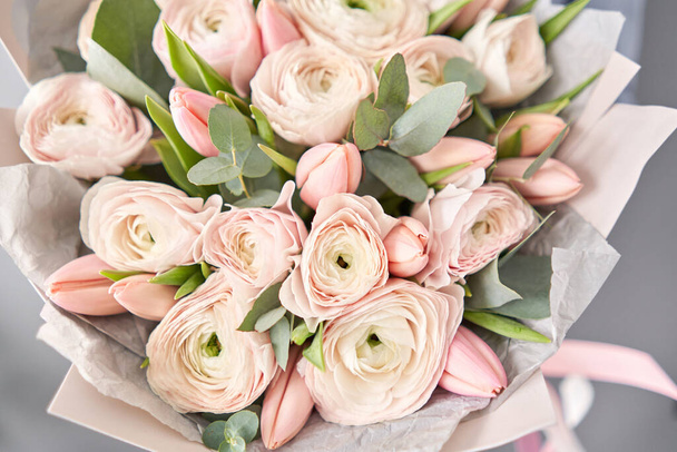 Ένα μάτσο ωχρές ροζ τουλίπες και ranunculus λουλούδια με πράσινο ευκάλυπτο. Η δουλειά του ανθοπώλη σε ανθοπωλείο. - Φωτογραφία, εικόνα