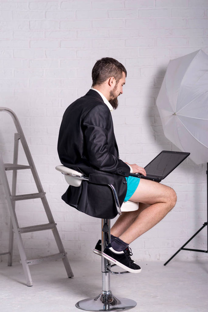 Mann in Jacke und kurzer Hose sitzt mit Laptop, dem Konzept der Fernarbeit. Workaholic arbeitet von zu Hause aus. Freiberufliche Tätigkeit. - Foto, Bild