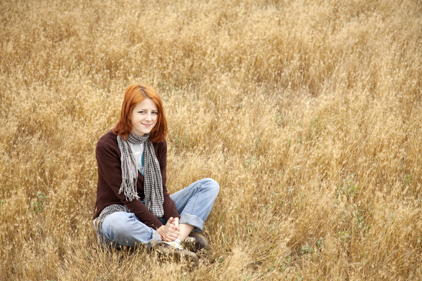 黄色の秋の草に座って美しい赤い髪の少女. - 写真・画像