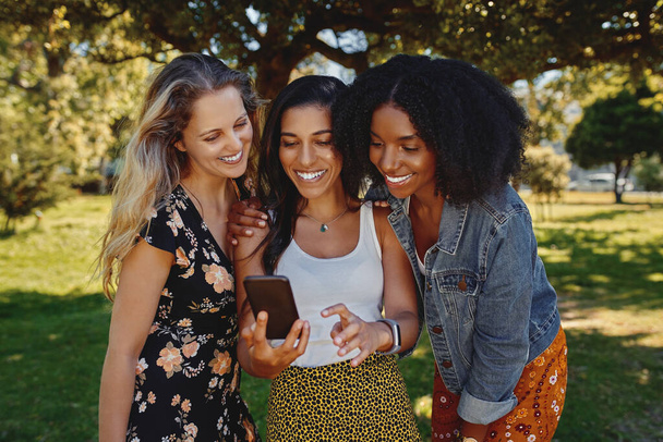 Portrait d'un groupe de jeunes amies diverses regardant quelque chose sur un téléphone intelligent dans le parc
 - Photo, image