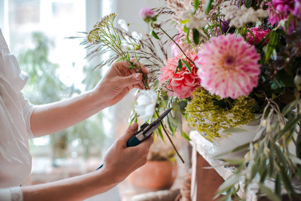 Female professional florist prepares the arrangement of wild flowers. Flower shop. Background concrete gray wall. Concept inspiration, floral, greetings, spring, ornament flowers. - 写真・画像