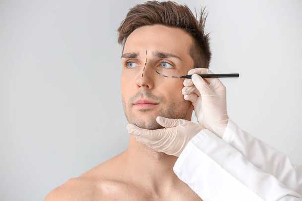 Plastic surgeon applying marking on male face against light background - 写真・画像