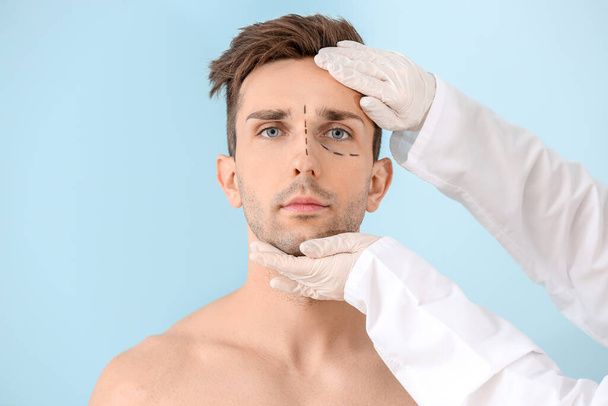 Plastic surgeon touching face of young man on color background - Photo, image