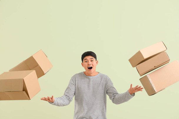 Asian man with moving boxes on color background - Photo, Image