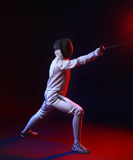 Toned photo of young fencer on dark background - 写真・画像