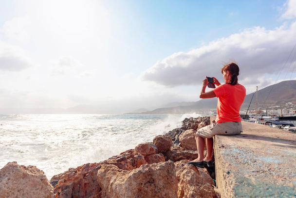 Mulher viajante maduro atraente usar telefone celular tirar uma foto de bela paisagem marinha. Espaço de cópia
. - Foto, Imagem