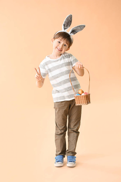 イースターエッグとウサギの耳を持つ小さな男の子は色の背景に勝利ジェスチャーを示しています - 写真・画像