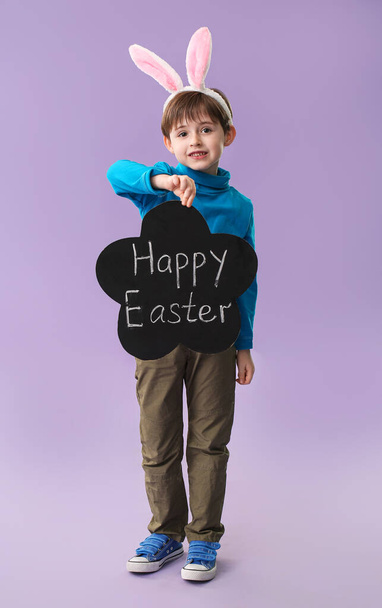 Kleiner Junge hält Kreidetafel mit dem Text HAPPY OSTER auf farbigem Hintergrund - Foto, Bild