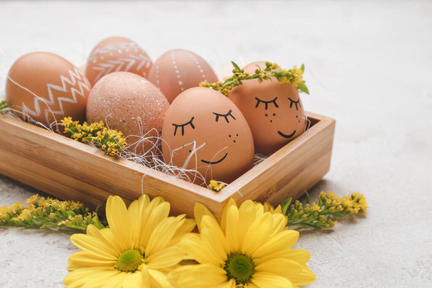 Box with beautiful Easter eggs and flowers on light background - Photo, Image