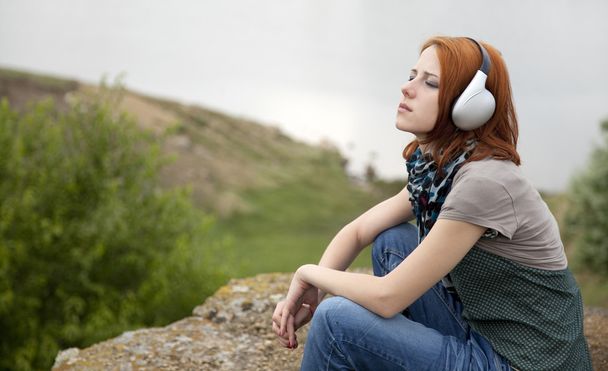junges Modemädchen mit Kopfhörern am Felsen am See. - Foto, Bild