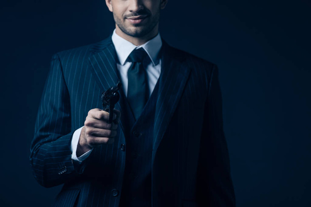 Vista recortada de gángster apuntando arma y sonriendo sobre fondo oscuro
 - Foto, Imagen