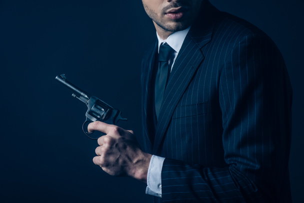 Cropped view of gangster with revolver on dark blue - 写真・画像