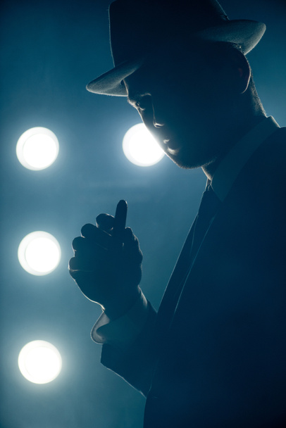 Silhouette eines Mafioso mit Zigarre und Blick in die Kamera auf dunklem Hintergrund - Foto, Bild