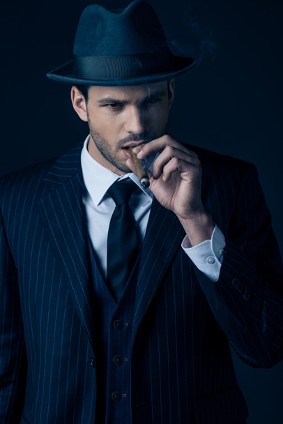 Front view of pensive mafioso smoking cigar on dark blue background - Photo, Image
